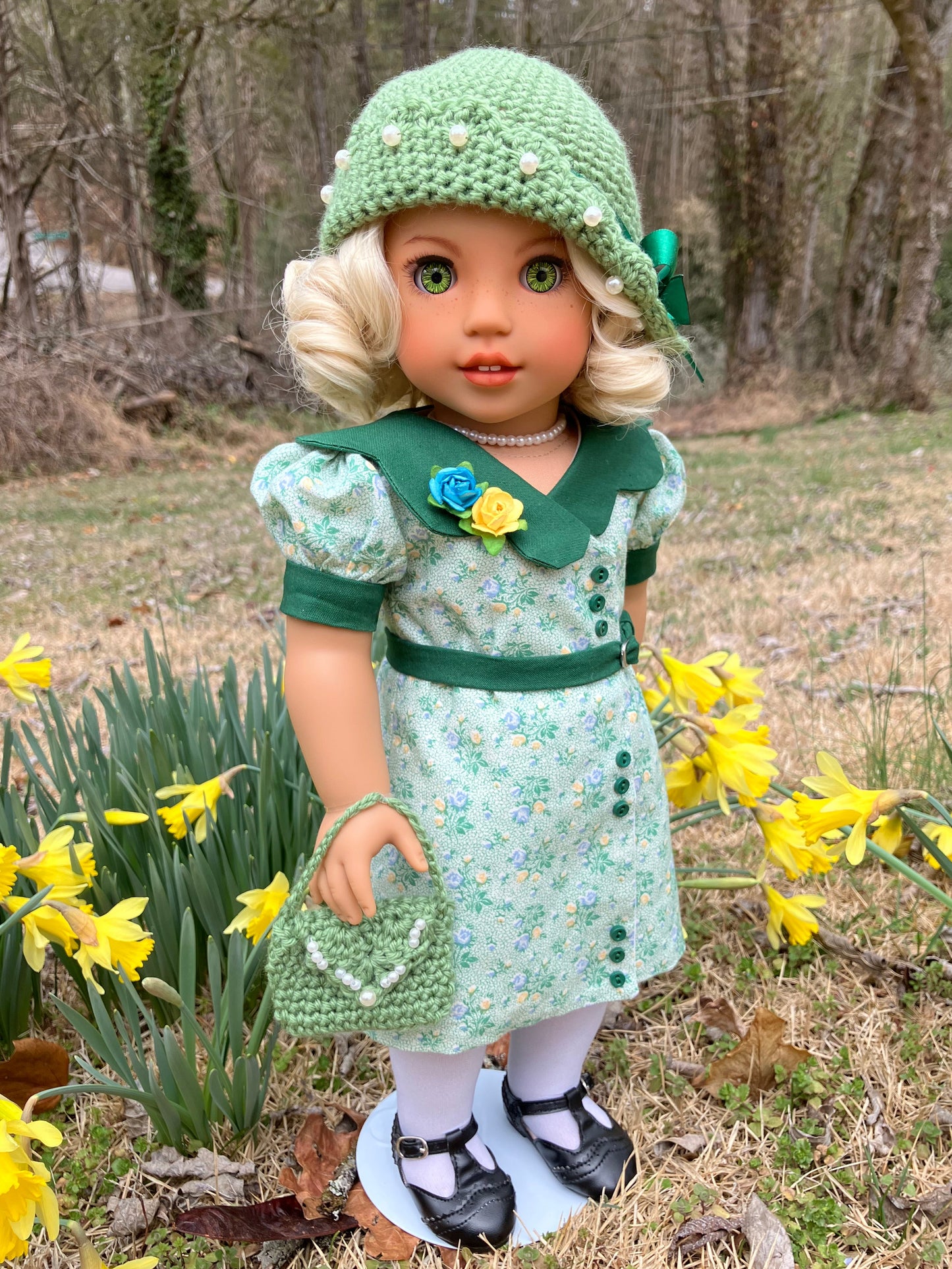 Doll in a green dress and hat standing among yellow flowers outdoors.