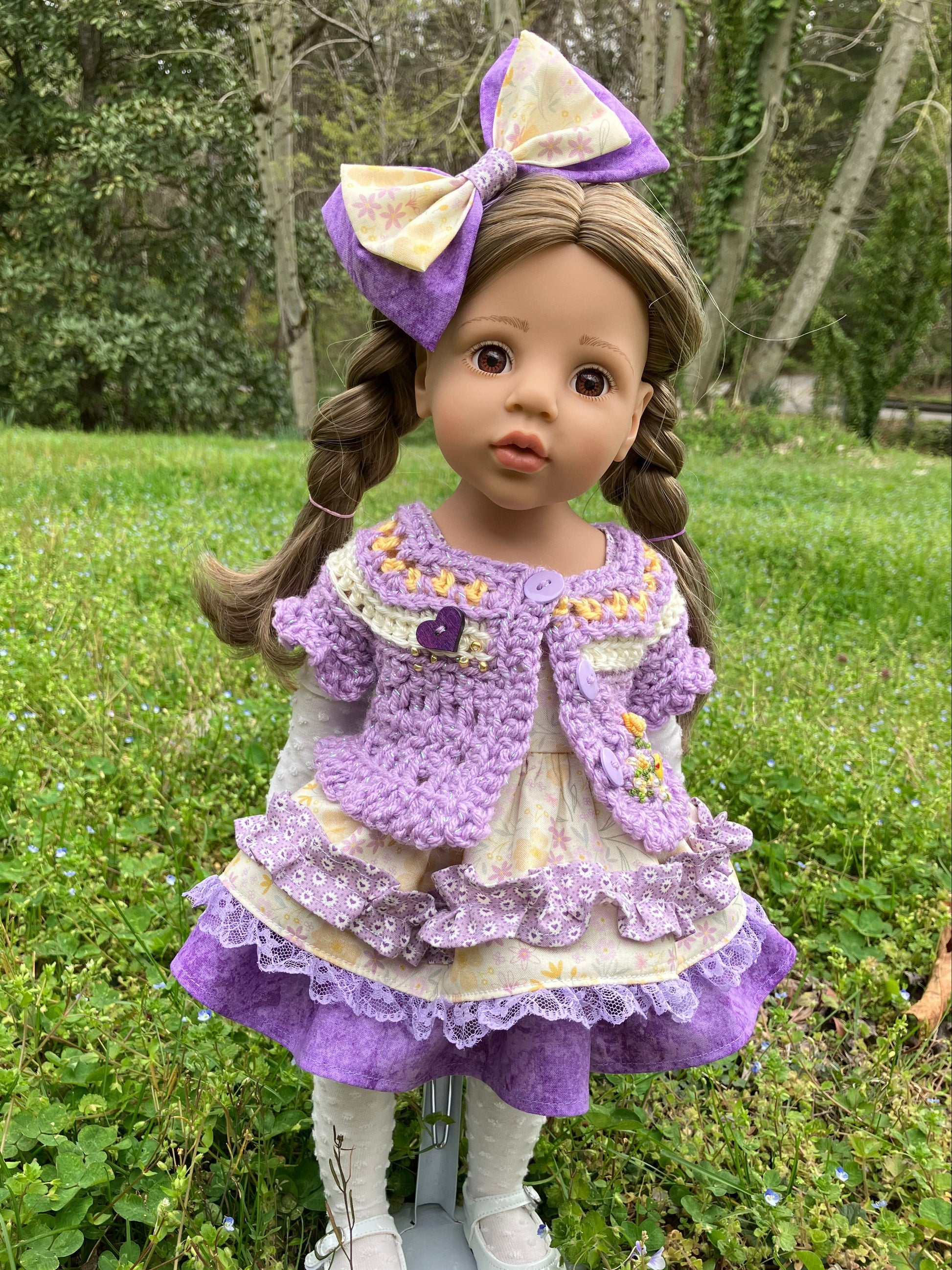 Doll in a purple dress with a large bow standing outdoors on grass